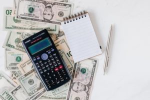 Calculator and notepad displayed on top of a table with money: how to determine how much your financial advisor business is worth